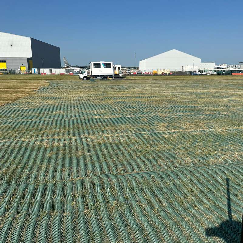 Side view of green mesh installation near white industrial tents used for operational support at the car park.