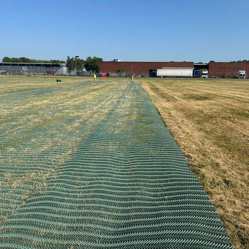 Angled shot of mesh-covered ground leading toward temporary buildings and airport surroundings.
