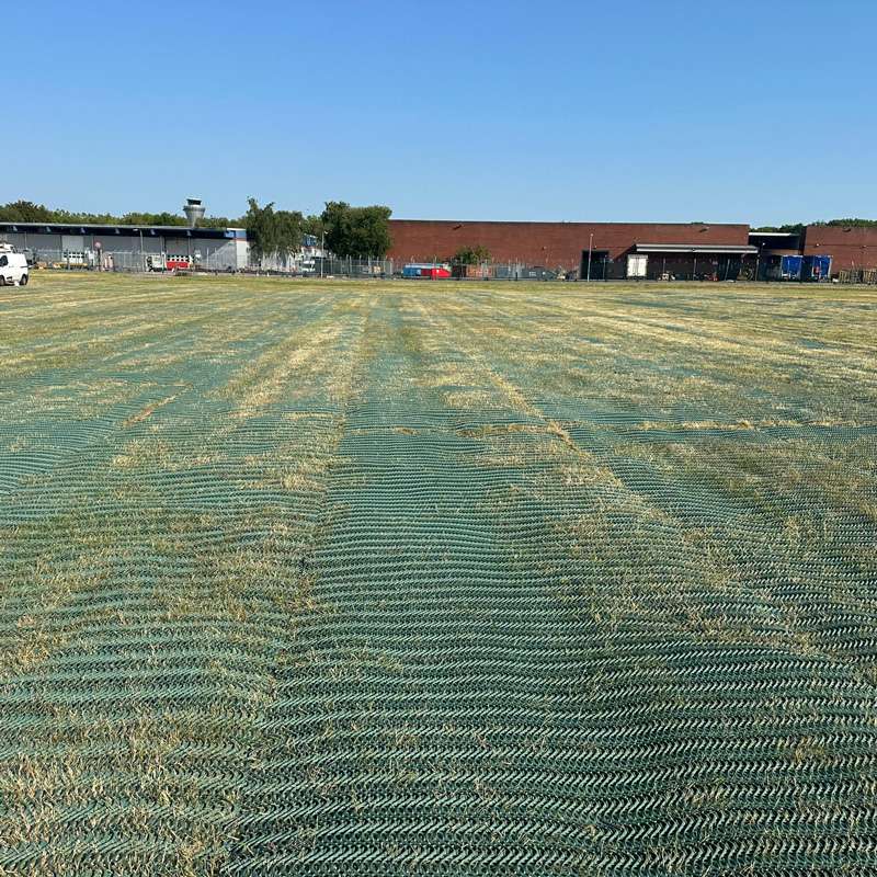 Reinforced grass surface leading toward red-brick buildings used for seasonal car park operations.