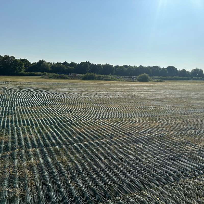 Close-up of green mesh laid diagonally across open field, showing structured installation near the site boundary.