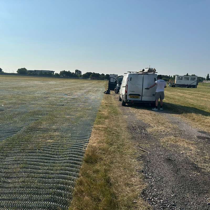 Grass-reinforced car park edge with gravel access lane and parked service vehicles at the airport car park