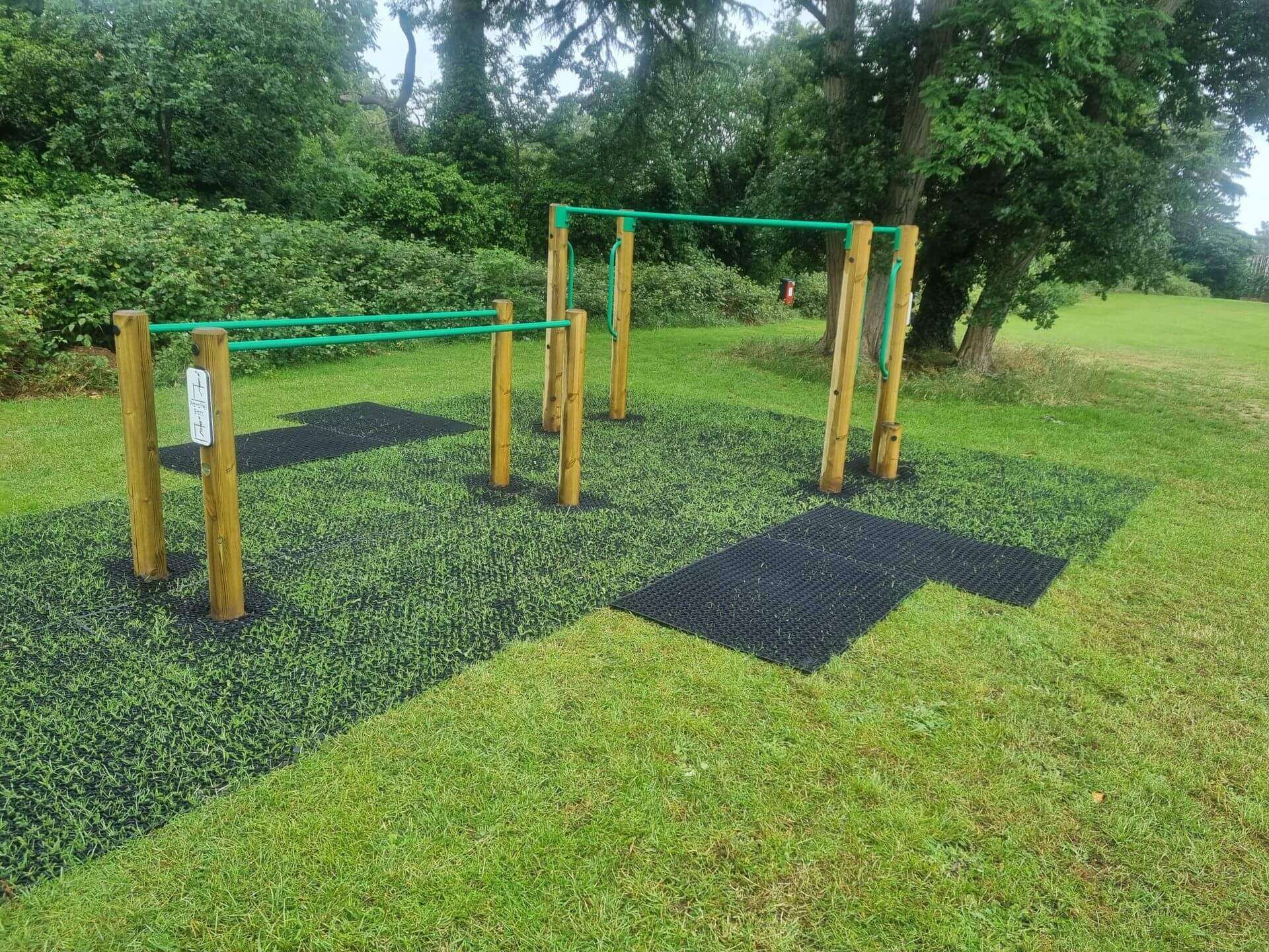 Playground safety grass mats with grass growing through around outdoor fitness equipment